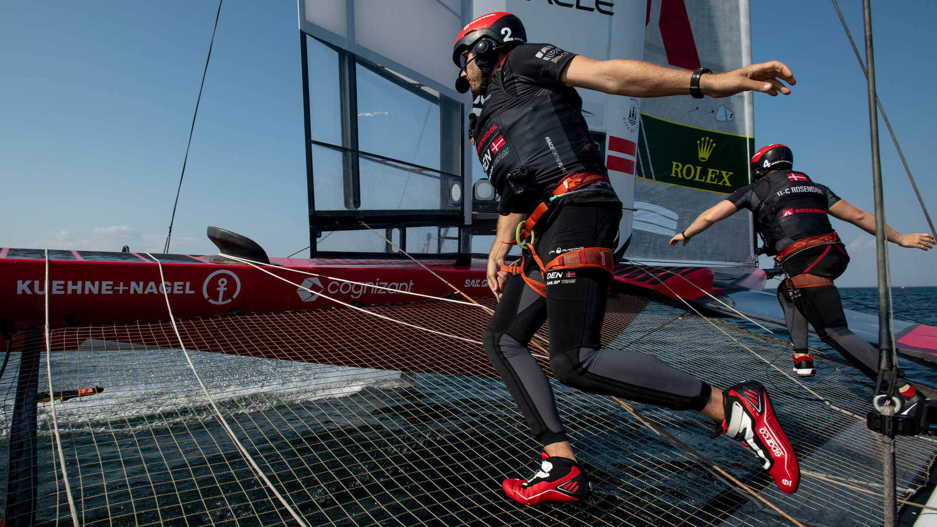 The Denmark SailGP Team athletes crossing the boat at high speeds during a tack.